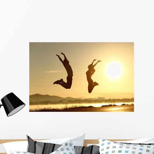 Fitness couple jumping happy at sunset Wall Mural