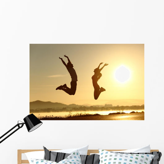 Fitness couple jumping happy at sunset Wall Mural
