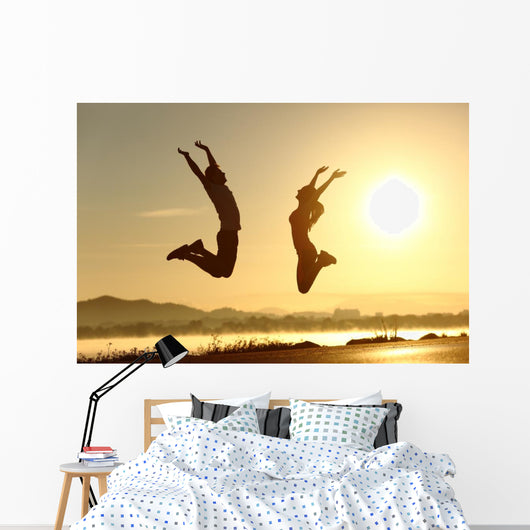 Fitness couple jumping happy at sunset Wall Mural
