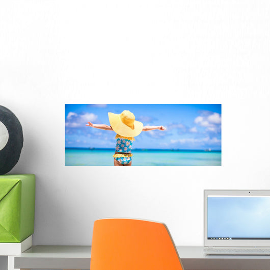 Little girl in big yellow hat on white sandy beach Wall Mural