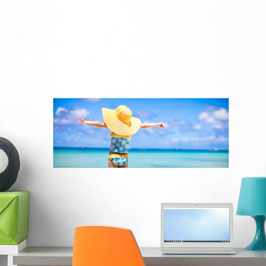Little girl in big yellow hat on white sandy beach Wall Mural
