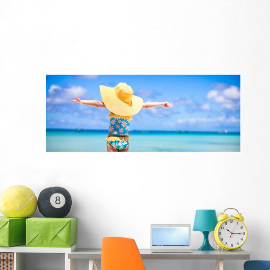 Little girl in big yellow hat on white sandy beach Wall Mural