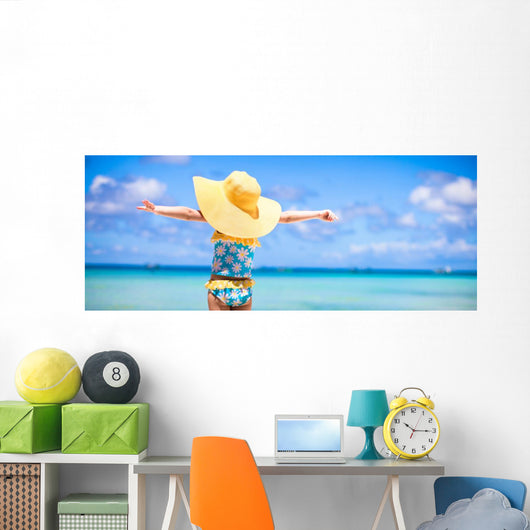 Little girl in big yellow hat on white sandy beach Wall Mural