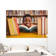 Cute boy reading book in library Wall Mural